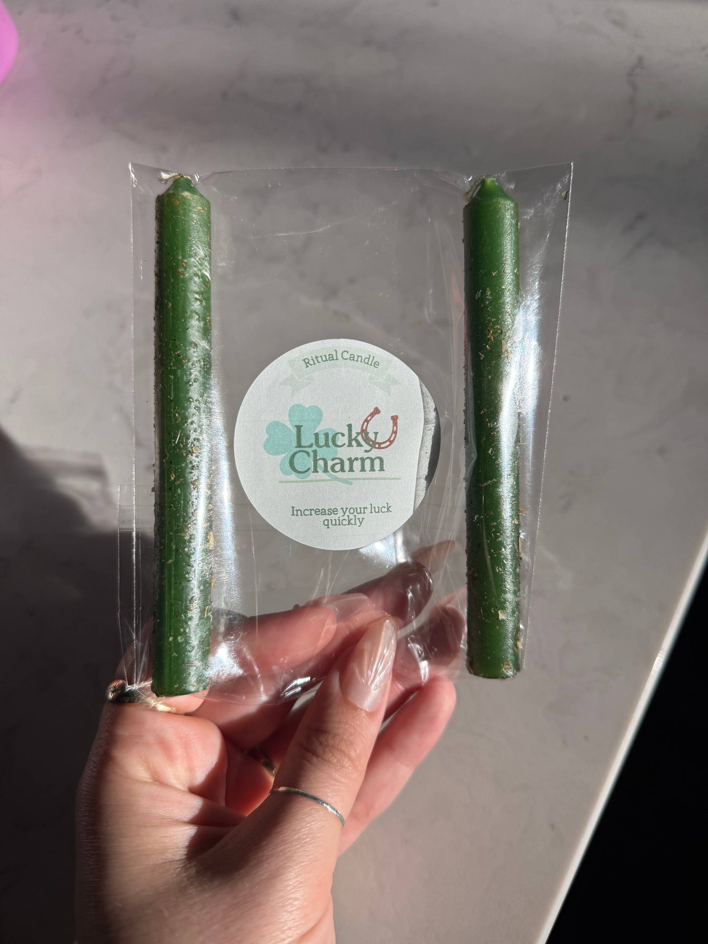 Two green candles in clear packaging with a 'Luck Charm' label held by a hand.