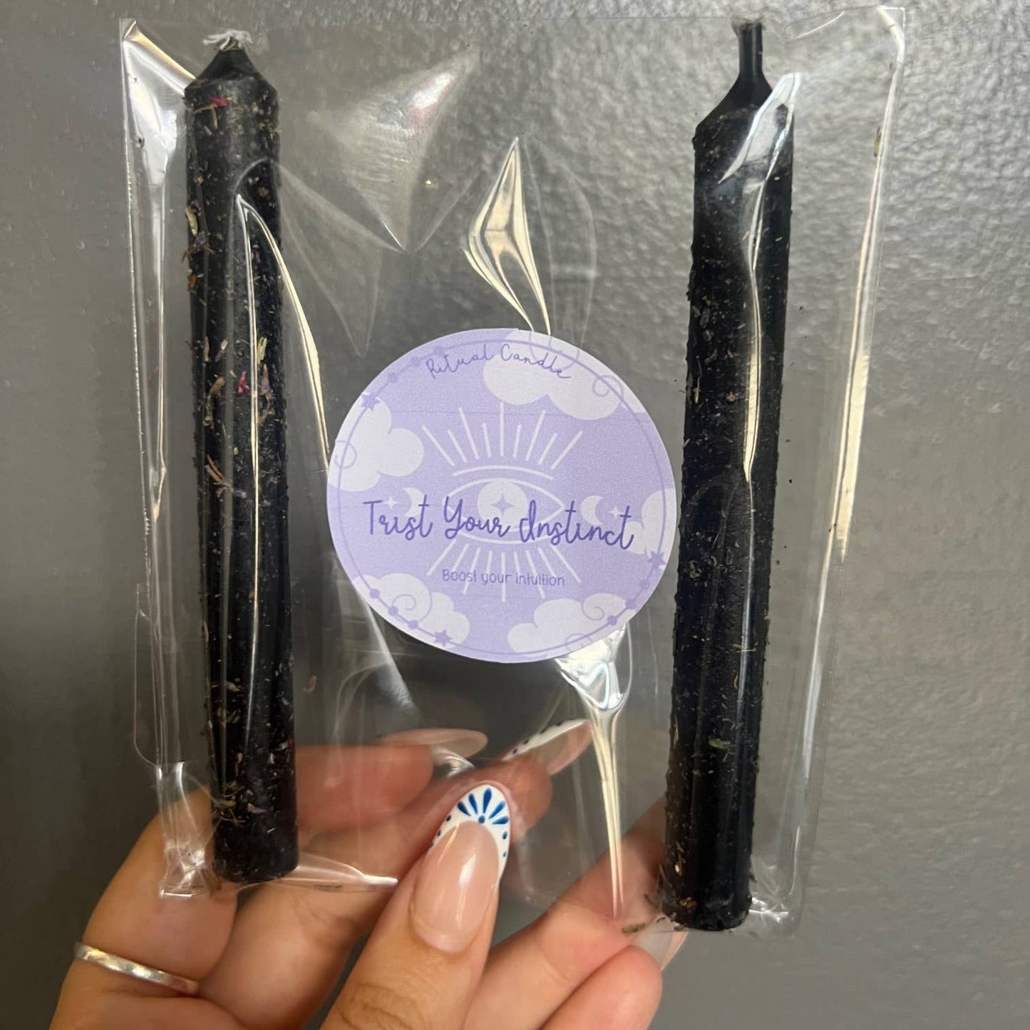 Two black candles in clear packaging with a purple label on a gray background