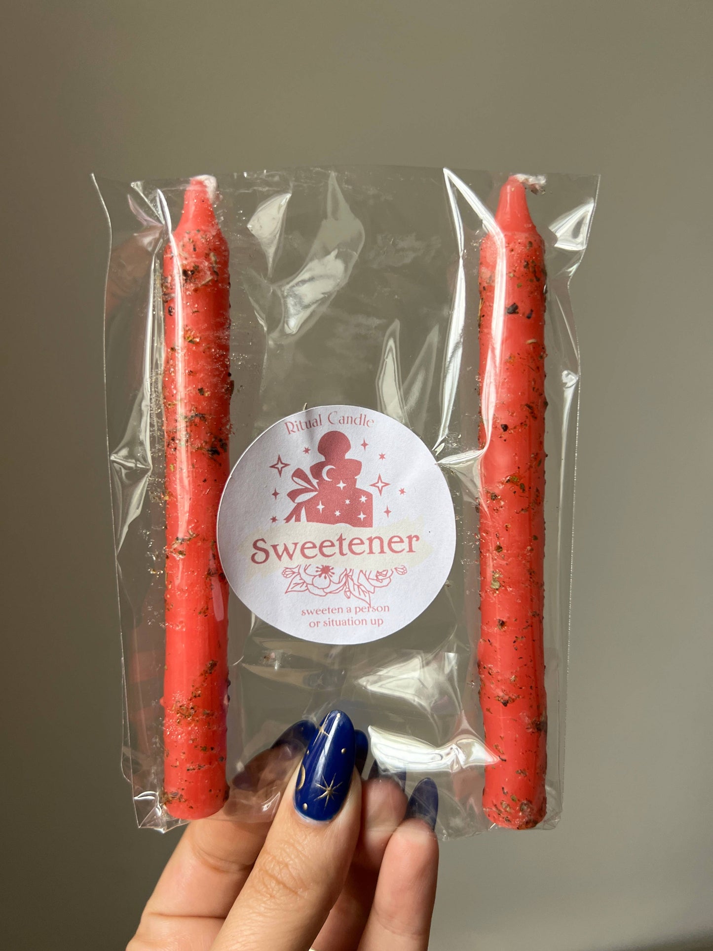 Two red candles in clear packaging with a 'Sweetener' label held by a hand.